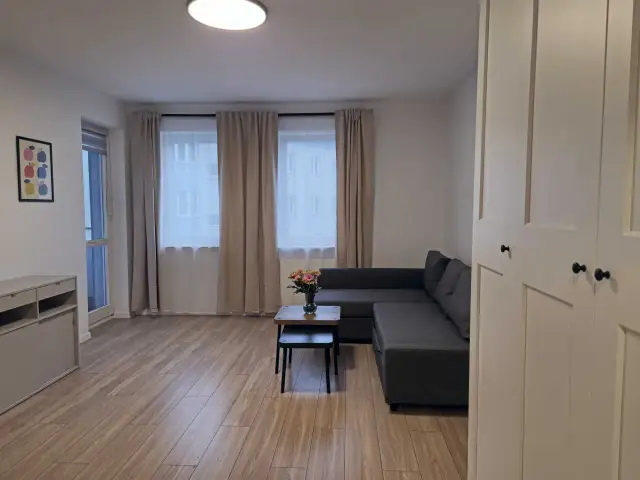 Nowoczesny salon z szarą kanapą, stolikiem kawowym z kwiatami i dużymi oknami.