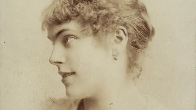 Portret Marii Wiśnowskiej z profilu, z delikatnym uśmiechem i kręconymi włosami.