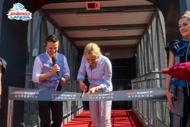 Kobieta przecina wstęgę z napisem "game expert HYPERION", mężczyzna trzyma mikrofon.