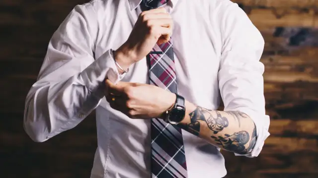 Mężczyzna w białej koszuli i krawacie poprawia mankiet, odsłaniając tatuaż na ramieniu. Czy prawnik może mieć tatuaż? Tak!