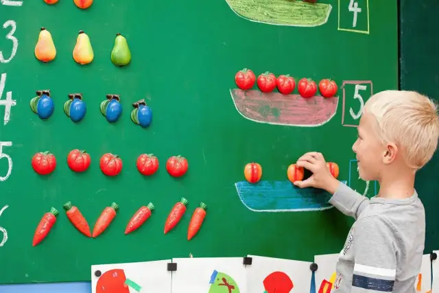 Chłopiec układa owoce na tablicy, ucząc się matematyki dla przedszkolaka. Kolorowe owoce pomagają w nauce liczenia.