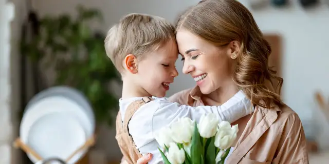 Uśmiechnięta mama i synek przytulają się, trzymając bukiet białych tulipanów. Idealny obrazek na Dzień Mamy.