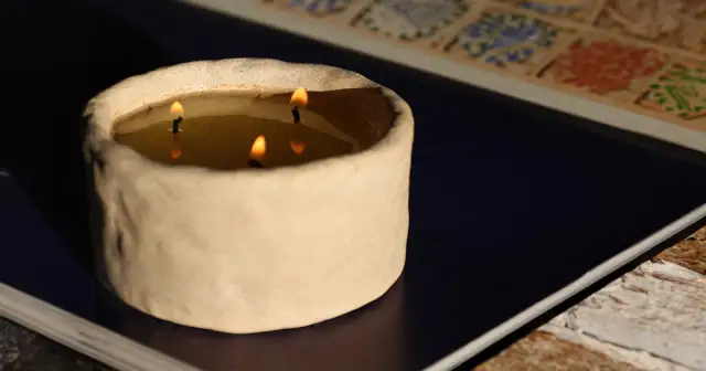 Świeca w ceramicznym naczyniu z trzema płonącymi knotami.