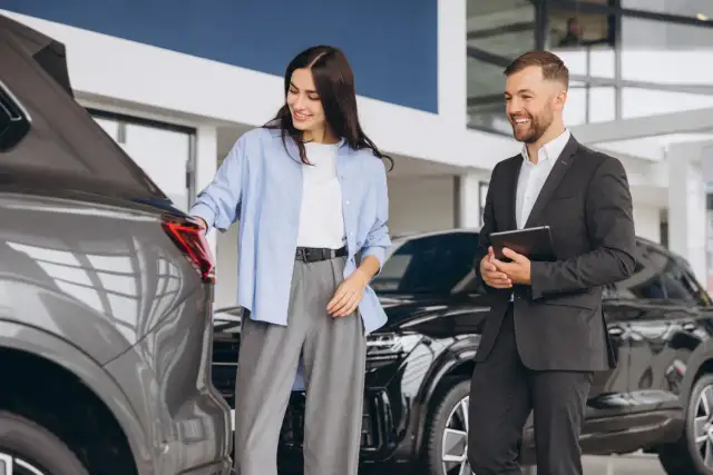 Kobieta ogląda samochód w salonie, obok stoi sprzedawca z tabletem.