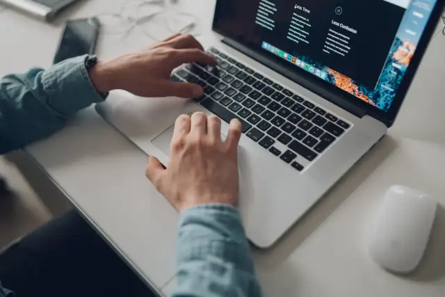 Osoba pracuje na laptopie, planując podróż z mbank konto wielowalutowe. Na biurku leży też myszka i telefon.