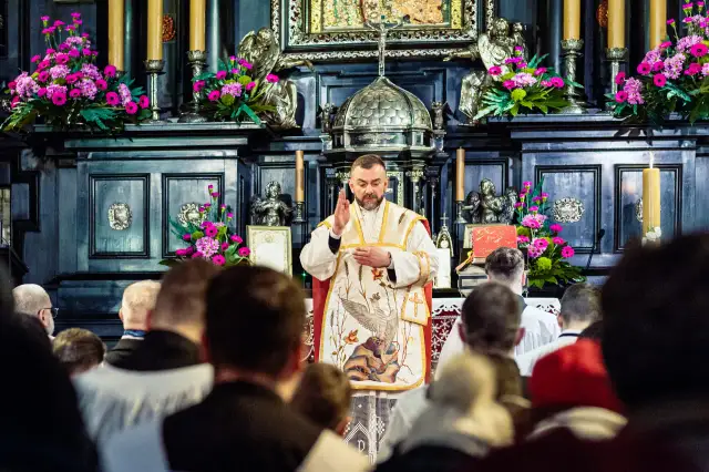 Kapłan w kościele, przed ołtarzem z kwiatami, błogosławi wiernych. W tle widać ozdobne zdobienia i świece. Jasna Góra intencje mszalne.