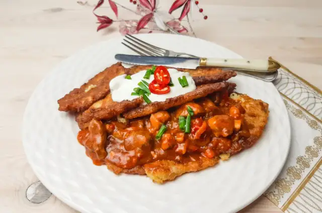 Pyszny placek po węgiersku z gulaszem, śmietaną i papryczką chili na białym talerzu.