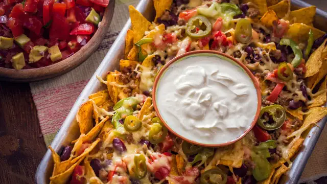 Nachos caseros con queso derretido, carne, frijoles, jalapeños y un tazón de crema agria.