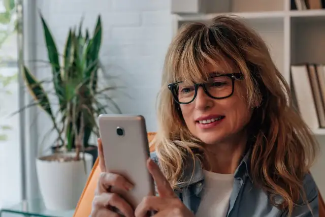 Kobieta w okularach przegląda telefon, być może szuka bratniej duszy na **Bumble w Polsce**.