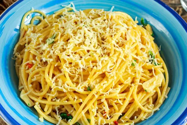 Porcja spaghetti z tartym serem i ziołami w niebieskiej misce.