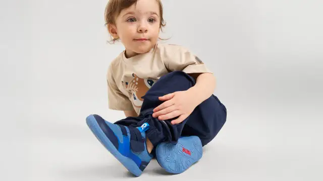 Małe dziecko w beżowej koszulce z jelonkiem i granatowych spodniach, w niebieskich butach.