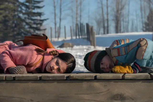 Dzieci leżą na drewnianej ławce, wpatrzone w dal. Ich twarze wyrażają zadumę, jakby snuły opowieści z pętli czasu, czekając na kolejne przygody.