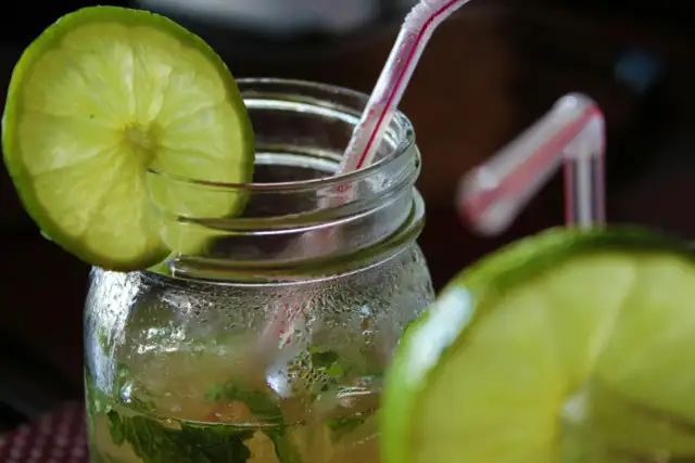 Orzeźwiający mohito drink, z widocznymi składnikami: limonką i miętą, w szklanym słoiku z rurką.