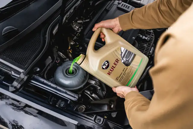Ręka wylewa zielony płyn chłodniczy z kanistra do zbiorniczka w komorze silnika samochodu.
