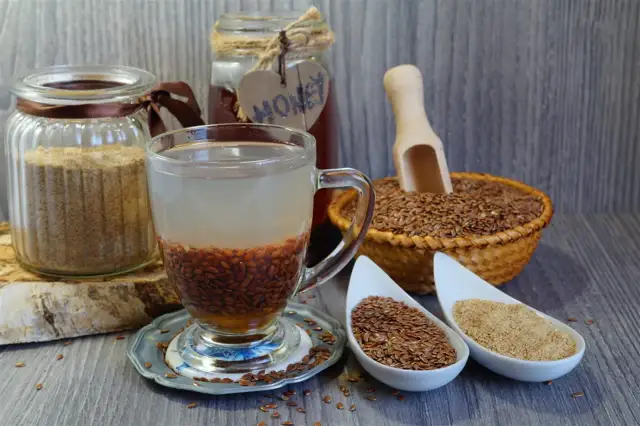 Naczynie z wodą i siemieniem lnianym do picia, obok słoik z mielonym siemieniem, koszyk z nasionami i miód.