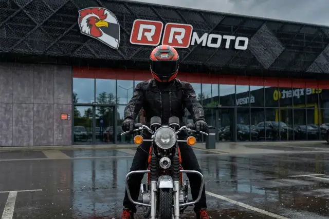Motocyklista w kurtce z membraną, która chroni przed deszczem, przed budynkiem RR MOTO.
