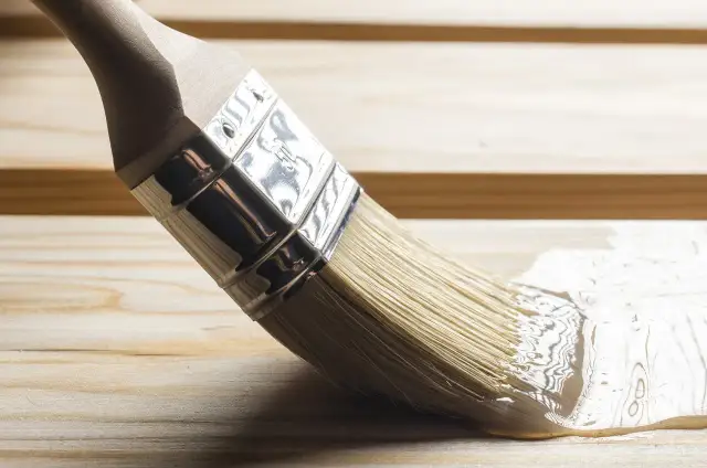 Pędzel rozprowadza lakier bezbarwny po drewnianej powierzchni, nadając jej połysk i ochronę.