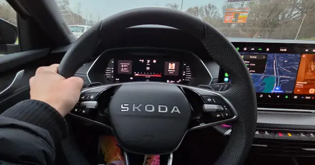Dłoń na kierownicy samochodu Skoda, widok na deskę rozdzielczą z mapą i temperaturą.