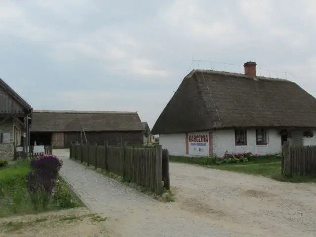 Zagroda Młynarska w Uniejowie: biały budynek z karczmą, drewniane zabudowania i ścieżka.