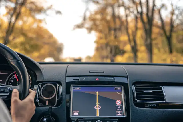 Widok z samochodu na jesienną drogę. Na ekranie nawigacji widać trasę, gdzie można zaktualizować nawigację.