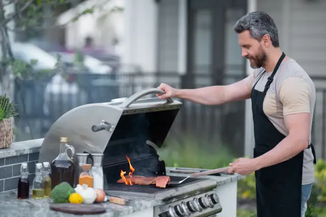 Mężczyzna w fartuchu grilluje łososia na grillu gazowym, pokazując, jak działa grill gazowy.