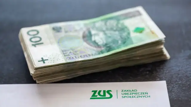 Stos banknotów 100 zł obok dokumentu ZUS. Może to symbolizować zarabianie na kontach bankowych lub oszczędzanie na przyszłość.