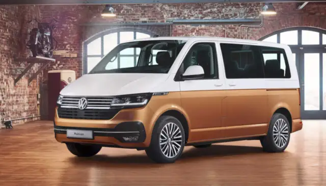 Biało-złoty bus osobowy Volkswagen Multivan w garażu z ceglaną ścianą.