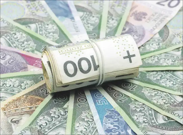 Zwijana rolka polskich banknotów 100 zł na tle innych banknotów.