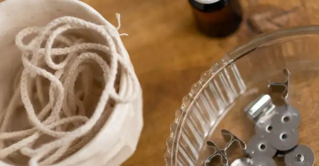 Biały sznurek w ceramicznym naczyniu i metalowe stopki do knotów w szklanej misce.