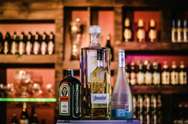Butelki Jägermeister, El Jimador, Absolut i Hipnotiq na tle baru.