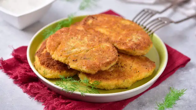 Kotlety z kalafiora w panierce na zielonym talerzu, udekorowane koperkiem.