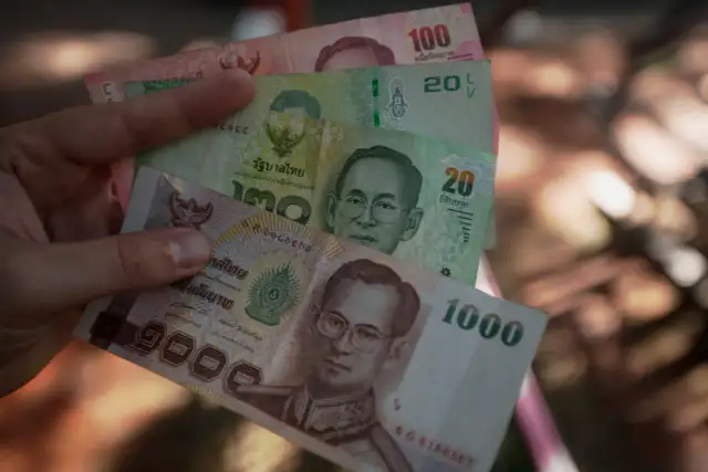 Ręka trzyma tajskie banknoty: 1000, 100, 20 bahtów. Planujesz podróż i zastanawiasz się, jakie dolary do Tajlandii zabrać? Lepiej wymienić na bahty.