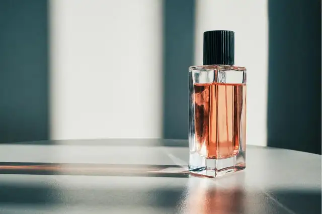 Eine Glasflasche mit rosafarbenem Parfum und schwarzem Deckel, beleuchtet von Sonnenlicht.