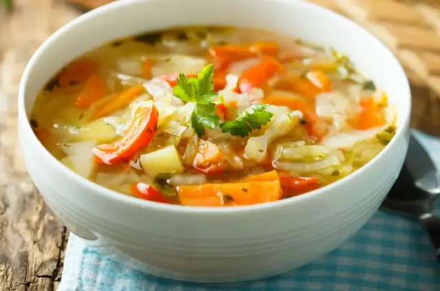 Rozgrzewająca zupa na przeziębienie z warzywami: marchewką, ziemniakami i kapustą, udekorowana natką pietruszki.