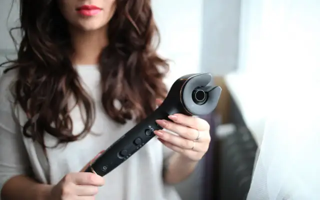 Kobieta trzyma czarną lokówkę automatyczną z elementami w kolorze złota.