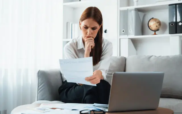 Zamyślona kobieta analizuje dokumenty, zastanawiając się, czy odpowiedź na pozew doręcza się pełnomocnikowi.