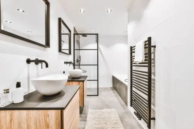 Nowoczesna łazienka z dwoma umywalkami, wanną i czarnym grzejnikiem łazienkowym drabinka, na którym wisi ręcznik.