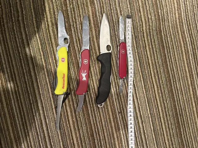 Cztery scyzoryki, w tym jeden z napisem "Rescue Tool", leżą obok miarki. Czy można przewozić nóż w bagażu rejestrowanym?