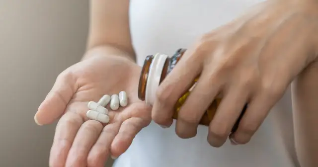 Dłoń wysypuje białe kapsułki z brązowej buteleczki. Czy to jakieś leki na zaniki pamięci?