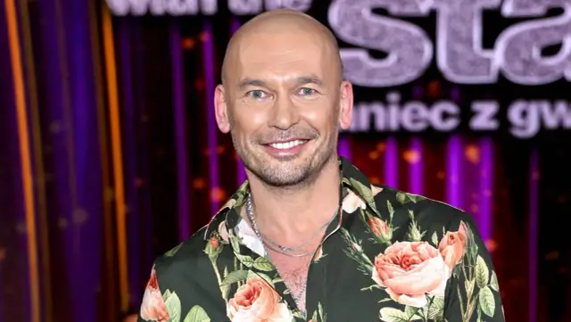 Tomasz z "Tańca z Gwiazdami" w kwiecistej koszuli, uśmiechnięty na tle sceny.