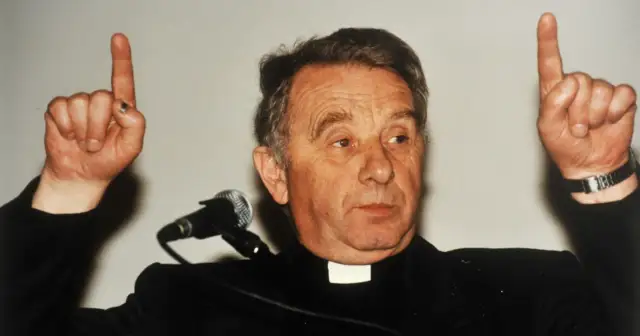 Ksiądz, autor historii filozofii po góralsku, podnosi dwa palce, jakby coś wyjaśniał.