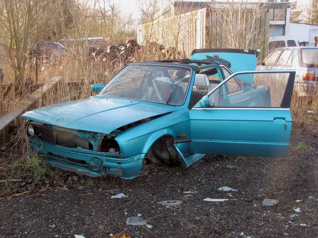Turkusowy, zniszczony samochód na złomowisku. Drzwi i maska otwarte, jakby ktoś właśnie zaczął zastanawiać się, jak zezłomować auto.