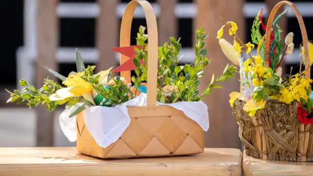 Inspiracja, jak udekorować koszyczek wielkanocny: bukszpan, żółte kwiaty, zielone i kolorowe pisanki tworzą wiosenną kompozycję.