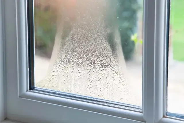 Skroplona szyba okienna, widoczna wilgoć na ścianie przy oknie. Krople wody tworzą wzory na szkle.
