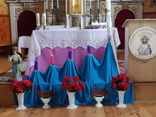 Ołtarz kościelny udekorowany na adwent: świece, kwiaty i figurka.