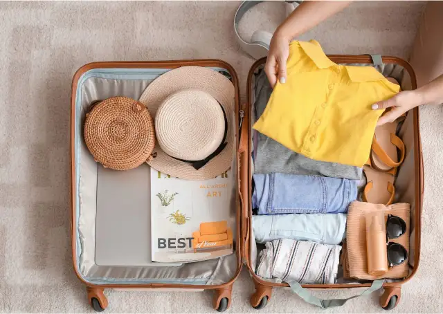 Otwarta walizka z ubraniami, kapeluszami, okularami przeciwsłonecznymi i kosmetykami.