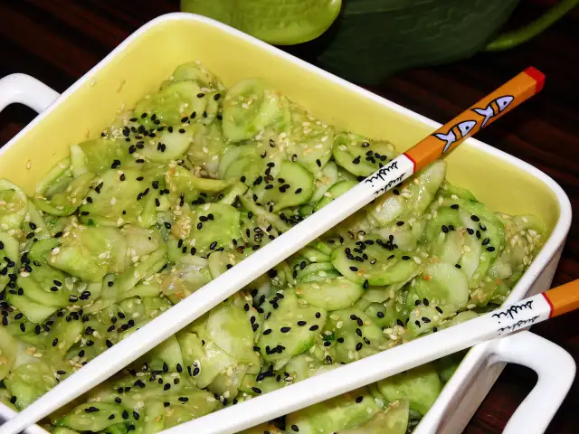 Pyszne ogórki po japońsku, posypane czarnym i białym sezamem, gotowe do jedzenia pałeczkami z motywem sushi.