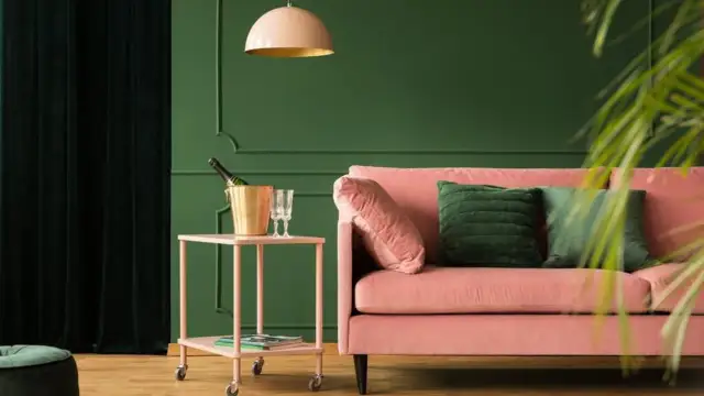 Różowa kanapa i złoty kubełek na szampana na stoliku. Wnętrze w odcieniach zieleni, gdzie kolory metali dodają elegancji.