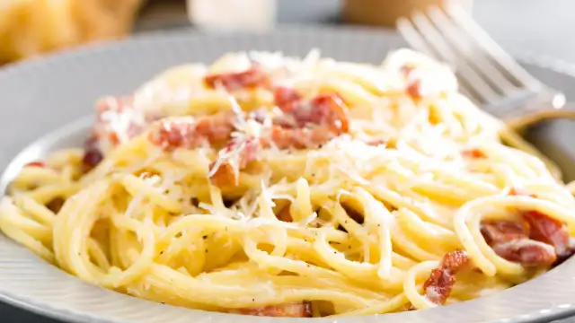 Spaghetti alla carbonara z boczkiem i parmezanem na szarym talerzu.