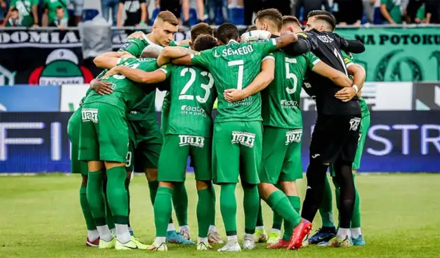 Piłkarze w zielonych strojach tworzą zwarty krąg na boisku.